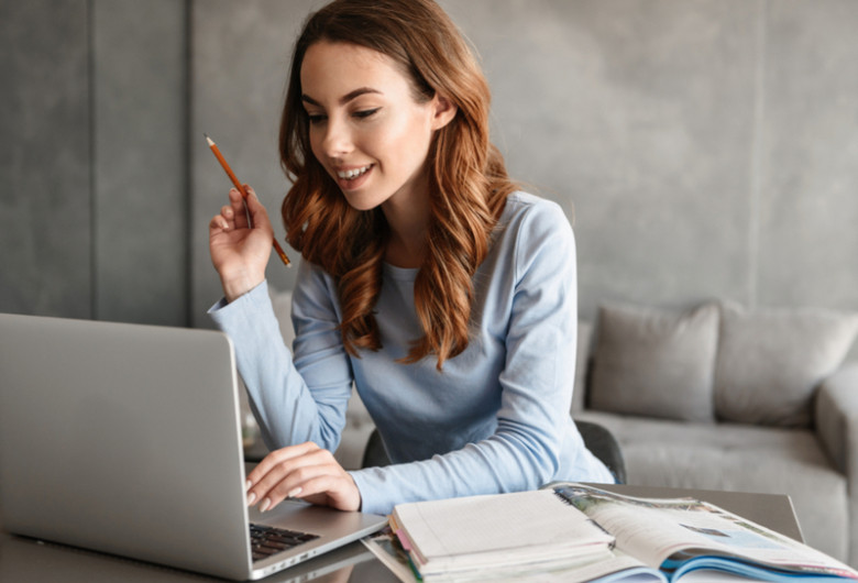 Tânără studentă sau elevă care se uită în laptop sau calculator online făcând teleșcoală