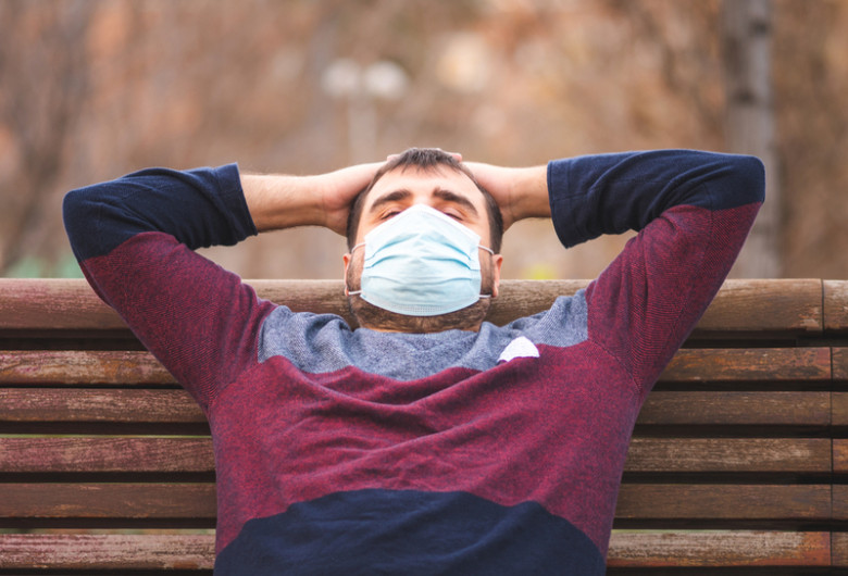 Bărbat mascat anti-COVID-19 se relaxează pe banca unui parc în zi liberă