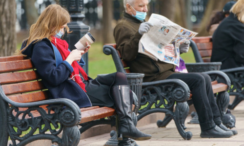 Oameni din Moscova, Rusia stau în parc pe băncuțe la relaxare, vacanță, zi liberă, sărbătoare legală, citesc ziar