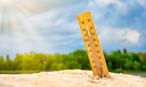 Weather thermometer in the sand against the sky showing a high ambient temperature