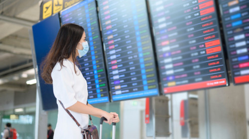 Femeie cu mască se uită la zboruri aeriene anulate în aeroport cu avioane pentru călătorii de turism