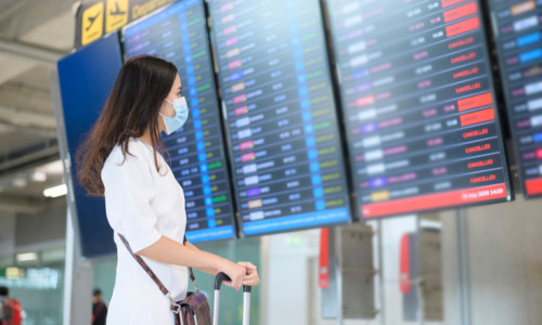 Femeie cu mască se uită la zboruri aeriene anulate în aeroport cu avioane pentru călătorii de turism