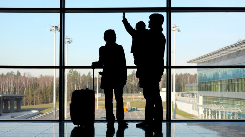 silhouette of young family with luggage standing near window in airport