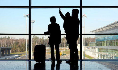 silhouette of young family with luggage standing near window in airport