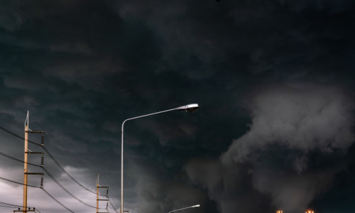 Stormy sky with street light pole and three-phase electric pylons. Stormy sky and dark clouds. Spotlights are open. Storm is coming. Bad weather. Climate change. Overcast sky. Beauty in nature.