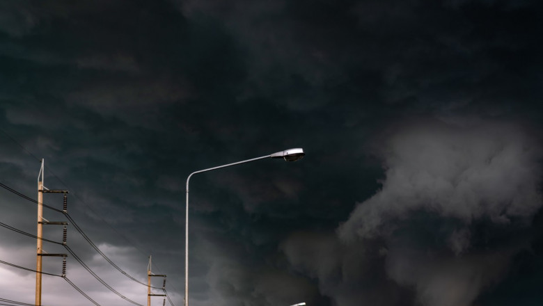 Stormy sky with street light pole and three-phase electric pylons. Stormy sky and dark clouds. Spotlights are open. Storm is coming. Bad weather. Climate change. Overcast sky. Beauty in nature.