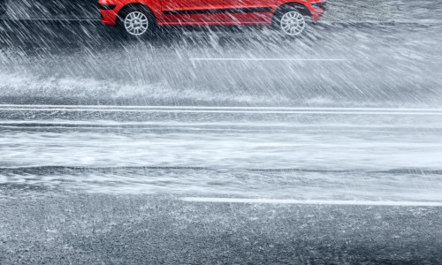 red car standing on a flooded road during heavy rain in the city