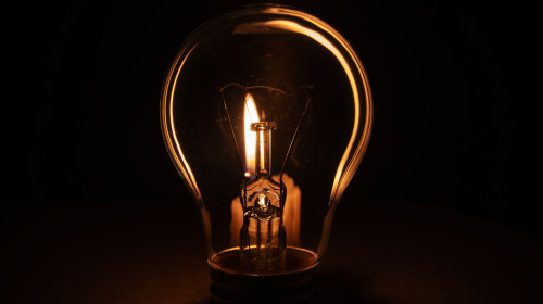 Light,Bulb,With,Lit,Candle,In,Background.,Blackout,City,,Electricity