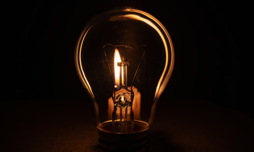 Light,Bulb,With,Lit,Candle,In,Background.,Blackout,City,,Electricity