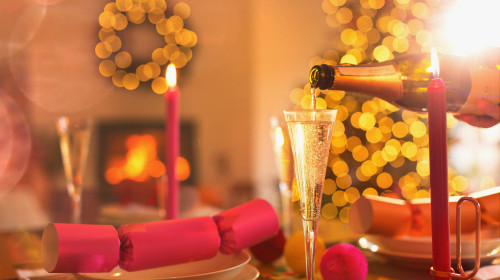 Pouring champagne into champagne flute on Christmas dinner table with Christmas cracker