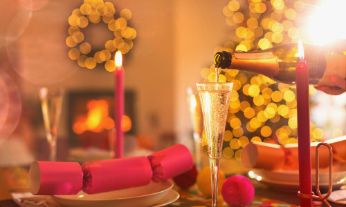 Pouring champagne into champagne flute on Christmas dinner table with Christmas cracker