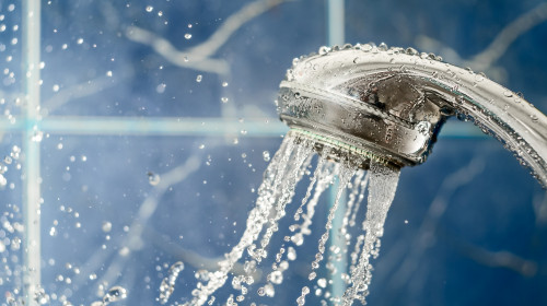Shower,Head,With,Water,Splashing,Out,On,Blue,Background,,Copy