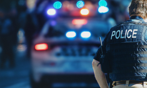 American,Policeman,And,Police,Car,In,The,Background