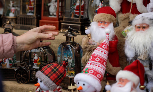 Shallow depth of field (selective focus) details with the hand of a woman reaching for Christmas gifts for sale in a Christmas market stall.