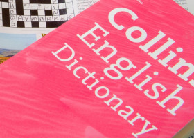 Close up Crossword Puzzle partially completed with Collins Dictionary and Rogets Thesaurus for assistance