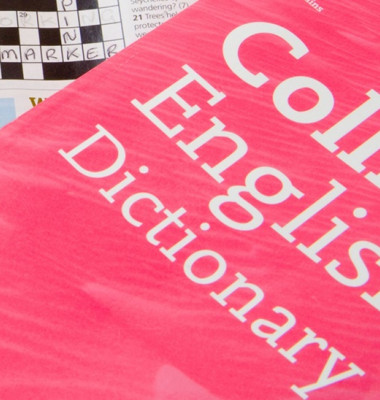 Close up Crossword Puzzle partially completed with Collins Dictionary and Rogets Thesaurus for assistance