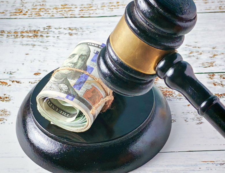 Cost of Justice: Rolled US Dollars Underneath Judge's Gavel on Rustic Surface