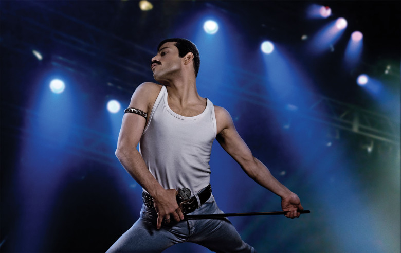 rami malek in rolul lui freddie mercury tine microfonul in mana si imita una din miscarile solistului queen
