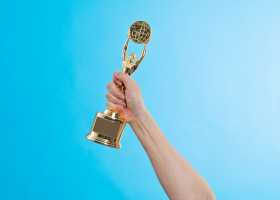 Hand,Holding,Golden,Statuette,Trophy,On,Blue,Background.