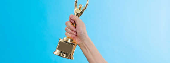 Hand,Holding,Golden,Statuette,Trophy,On,Blue,Background.