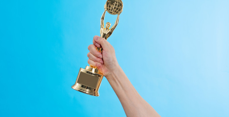 Hand,Holding,Golden,Statuette,Trophy,On,Blue,Background.