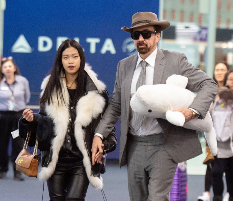 *EXCLUSIVE* Nicolas Cage holds hands with girlfriend Riko Shibata carrying a beluga whale plush toy upon arrival at JFK
