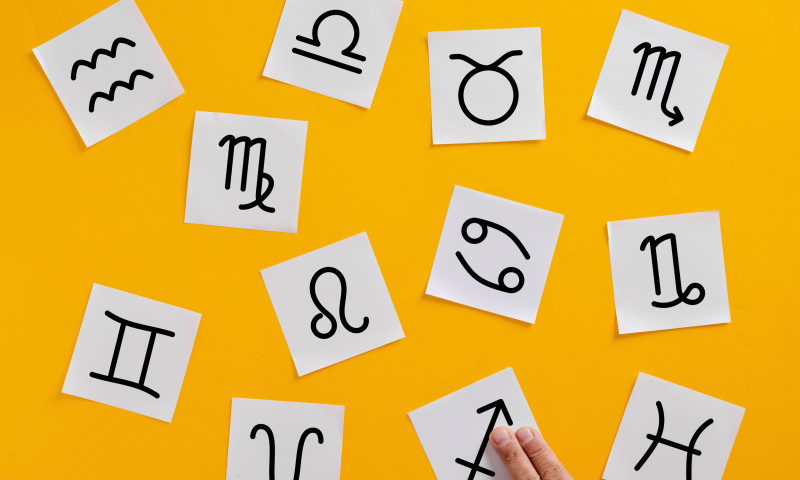 Hand of an astrologer skillfully arranging zodiac signs on a vibrant yellow background, capturing the essence of astrology and mysticism