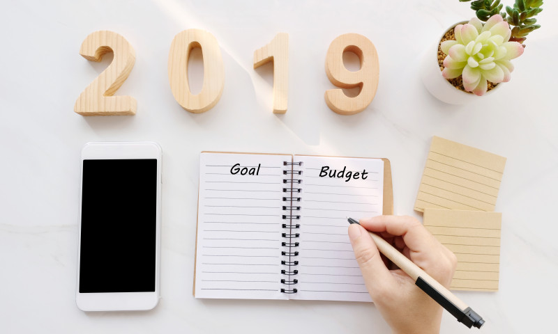 2019 goal and budget word on blank notebook paper background and smart phone on white marble background, financial concept, business strategy