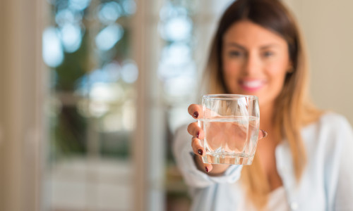 Beautiful young woman smiling while holding a glass of water at home. Lifestyle concept.