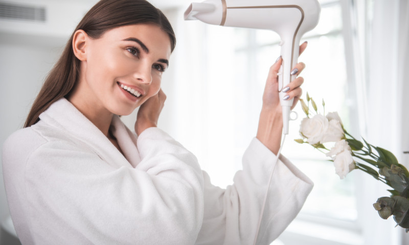 Cheerful woman drying hair with appliance indoor