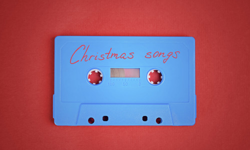 Blue audio cassette tape with christmas songs laying on red paper background.