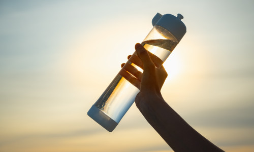 Human hand holds a water bottle against the setting sun.