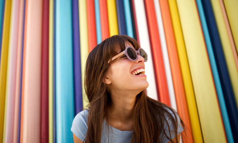Close up cheerful young woman laughing with sunglasses against colourful background