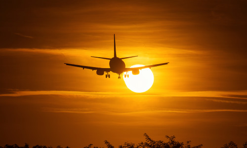 Silhouette of an air plane over the sun with beautiful red clouds in background