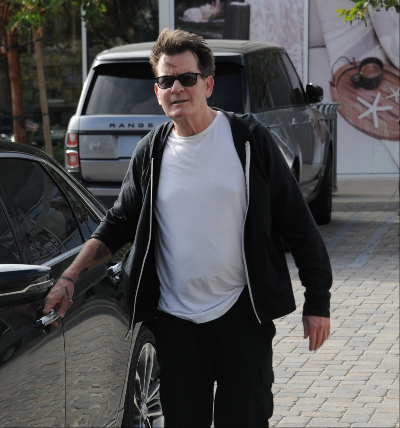 Charlie Sheen imbract in negru, cu un tricou alb urca intr-un bolid de lux