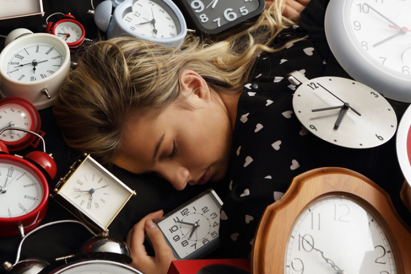 Femeie care doarme inconjurata de mai multe ceasuri desteptatoare