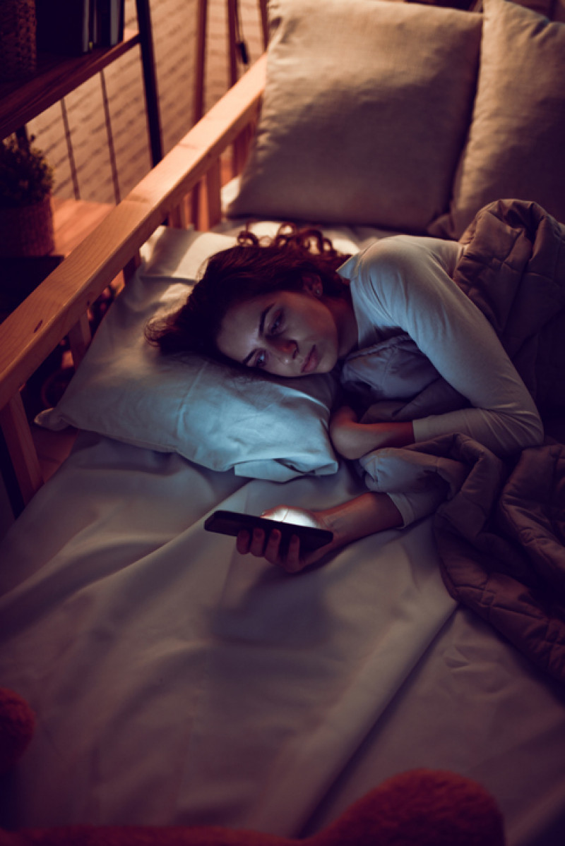 O femeie se uita intens la telefon in toiul noptii, are insomnii