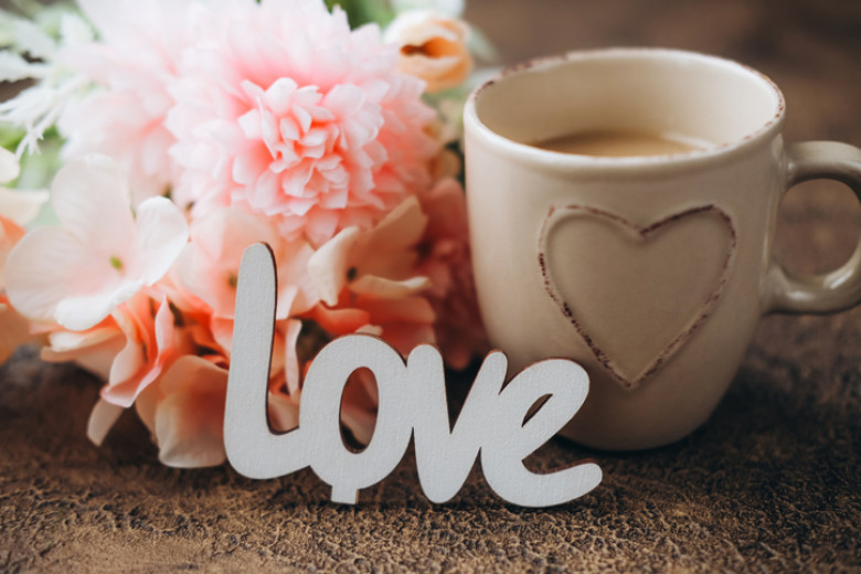 Word Love leaning on flowers and cup of coffee.