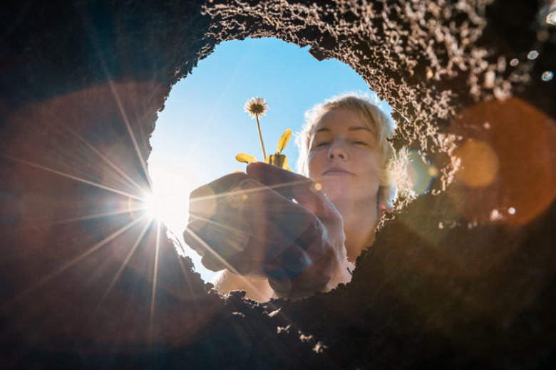 A young woman planting flower seedlings in the soil with a garden shovel on a sunny spring day. Gardening in your front or backyard