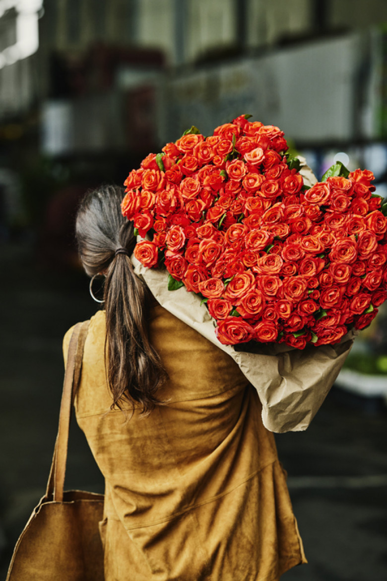 Medium shot woman carrying large bouquet of roses over shoulder