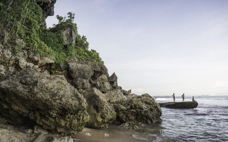 Three men on coastal rock at Panawa Beach, Bali, Indonesia