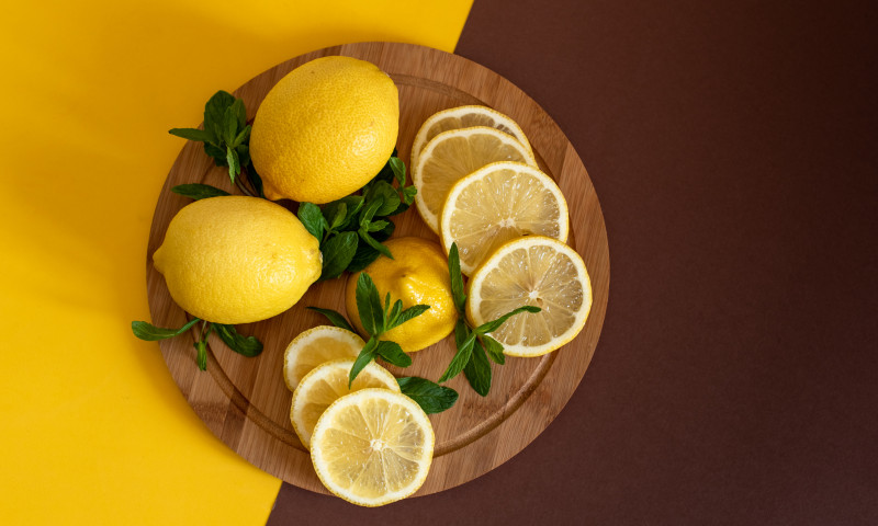 Board with cut lemons and zest on wooden table, closeup