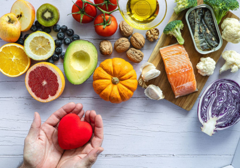 Two hands holding a red heart surrounded by healthy foods to prevent cancer and heart disease. Fresh fruits, vegetables and fish. Disease prevention.
