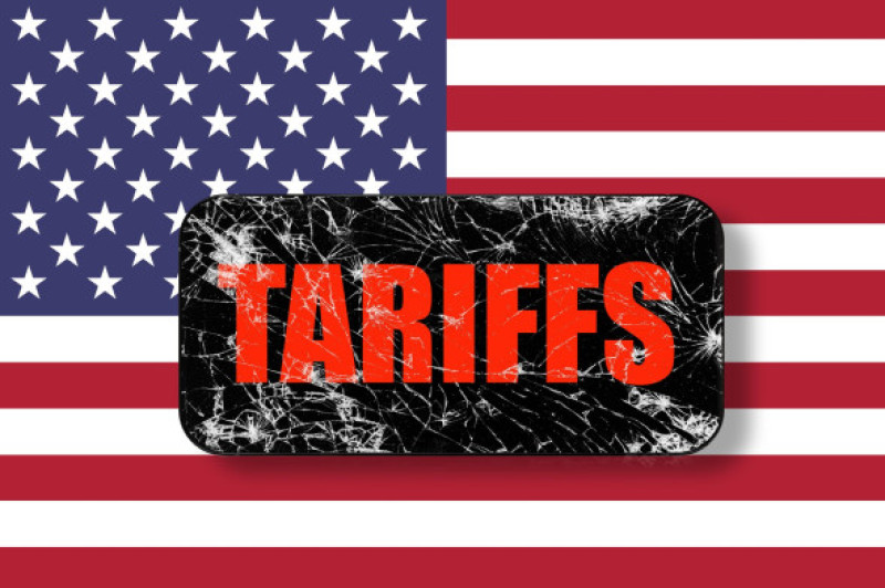 Black touch screen phone with cracked screen on USA flag background with word TARIFFS. Trade, duty, customs and tariffs war