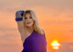 Loredana Groza, pe o plajă din Maldive, la apus, îmbrăcată într-o rochie cu crăpătură până la șold. Exprimă senzualitate și încredere fără limite