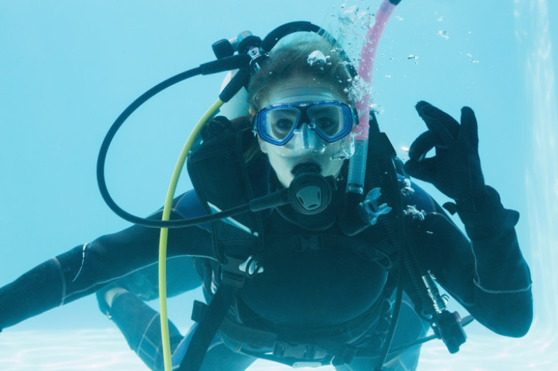 Woman on scuba training submerged in swimming pool making ok sign