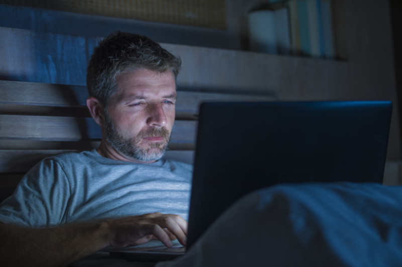 young attractive and relaxed internet addict man networking concentrated late at night on bed with laptop computer in social media addiction or workaholic businessman concept