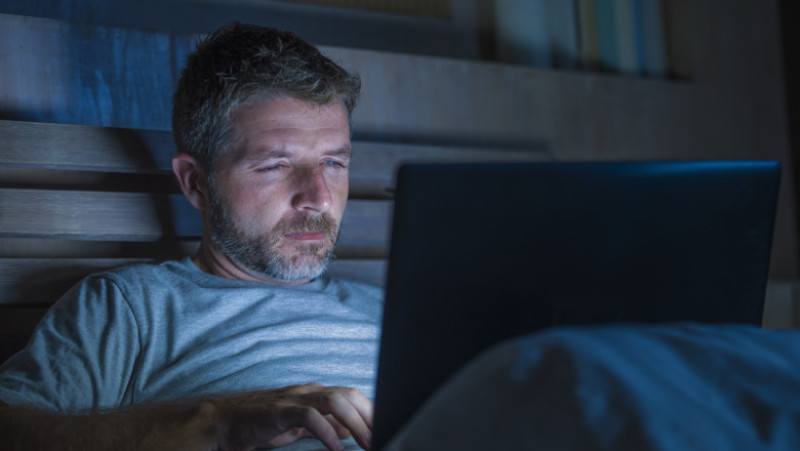young attractive and relaxed internet addict man networking concentrated late at night on bed with laptop computer in social media addiction or workaholic businessman concept