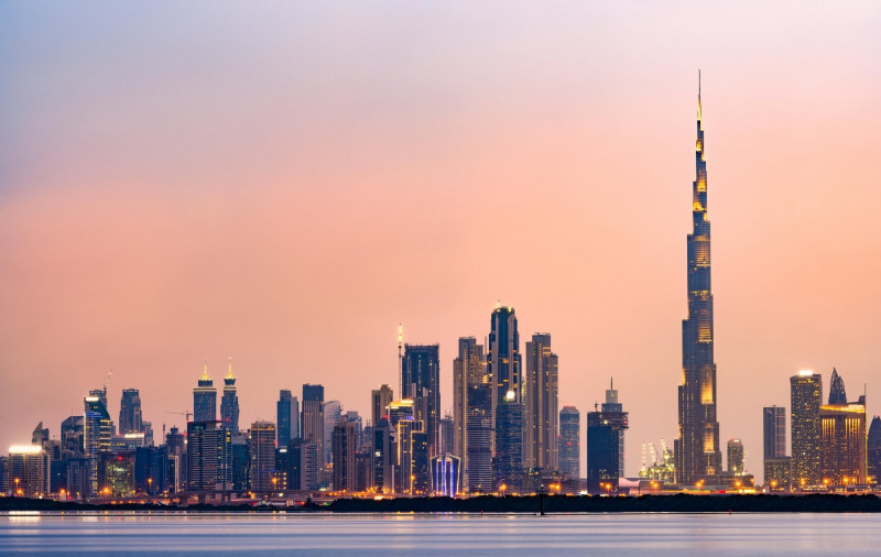 Stunning panoramic view of the illuminated Dubai skyline during sunset with beautiful shades of pink and orange colors.