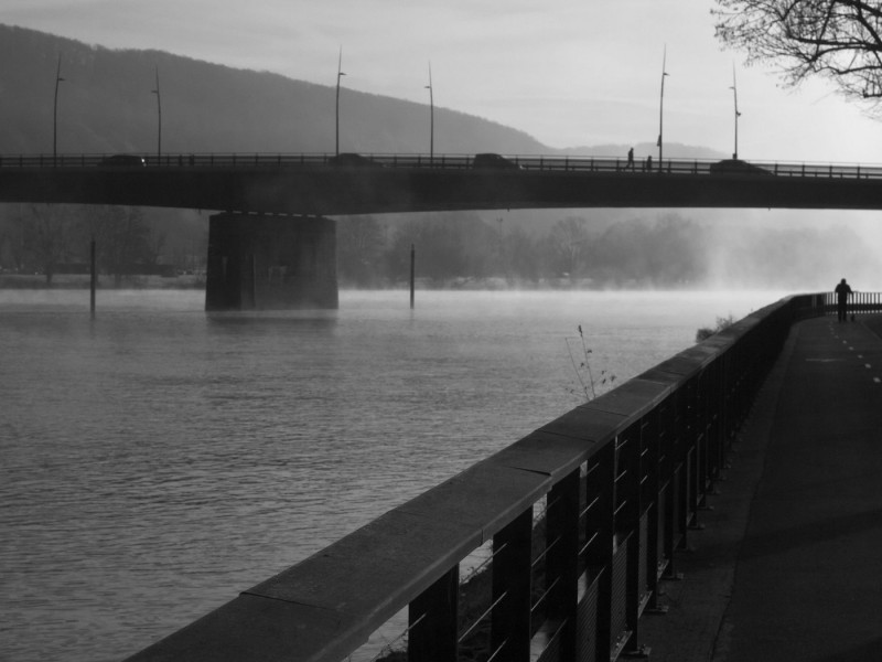 The River Seine at Vernon, Normandy, France. | Black and white image of a tranquil river scene with a bridge in the background and a person walking al